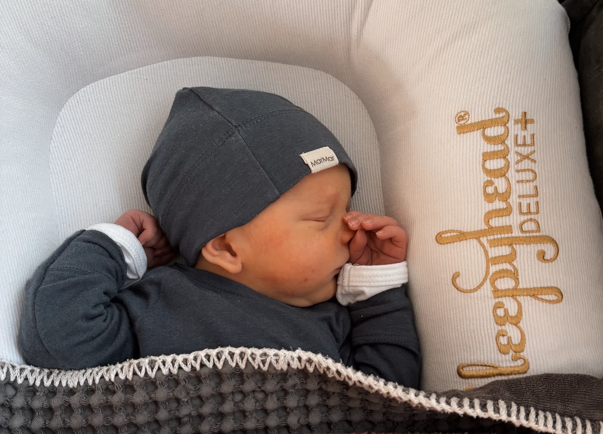 Pasgeboren Mees slaapt in een babynestje, met een donkerblauw mutsje op